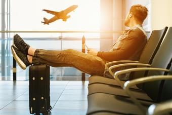 person in airport chair with feet up on suitcase